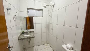 Um banheiro pequeno, com azulejos, pia, espelho e chuveiro.