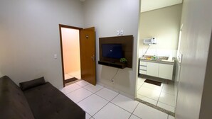 A living room with a sofa, a television mounted on the wall, and a kitchen area with cabinets and a microwave. - CONDOMÍNIO SONHARE - 104 (Anapolis)