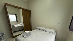 Un dormitorio con una cama, un espejo, un armario y un ventilador.