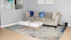 A living room with a beige sofa, a white coffee table, and a blue and white patterned rug. - Modern Style Minimalistic Home! (Dallas)