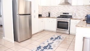 A modern kitchen with white cabinets, stainless steel appliances, a tiled backsplash, and a blue patterned rug. - Modern Style Minimalistic Home! (Dallas)