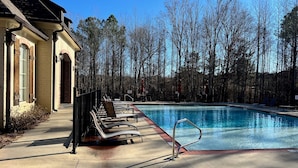 Ein Pool mit Liegestühlen, ein Gebäude mit Backsteinfassade und bewaldeter Hintergrund.