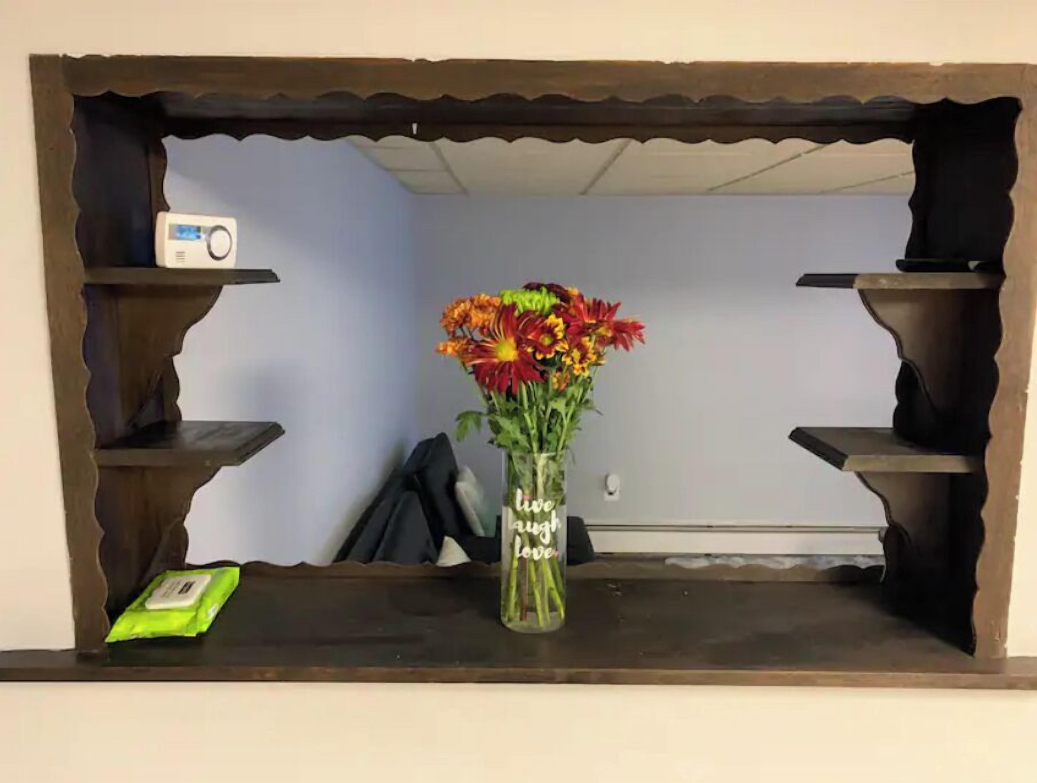 Une étagère en bois sur laquelle sont posés un vase de fleurs et un petit appareil.