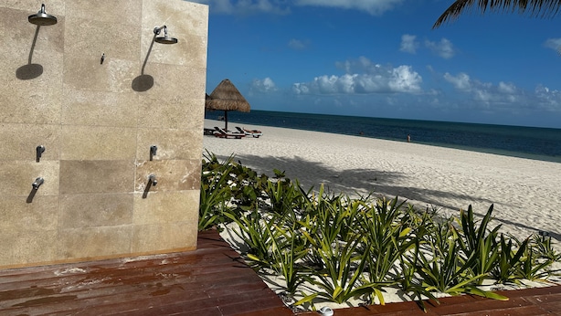 A beachside area with a tiled wall, a thatched umbrella, and a wooden deck. - Luxury 3 Bedroom Beachfront Cancun Vila  (Punta Sam)