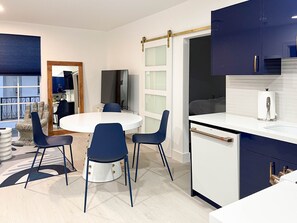 A modern kitchen with white cabinets, a white countertop, and blue chairs around a round table. - Marley SoFi: Walk to beach, 3 Beds, Heated POOL (Miami Beach)