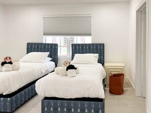 A twin bedroom with two beds, a window with blinds, a nightstand, and a brown bag. - Marley SoFi: Walk to beach, 3 Beds, Heated POOL (Miami Beach)