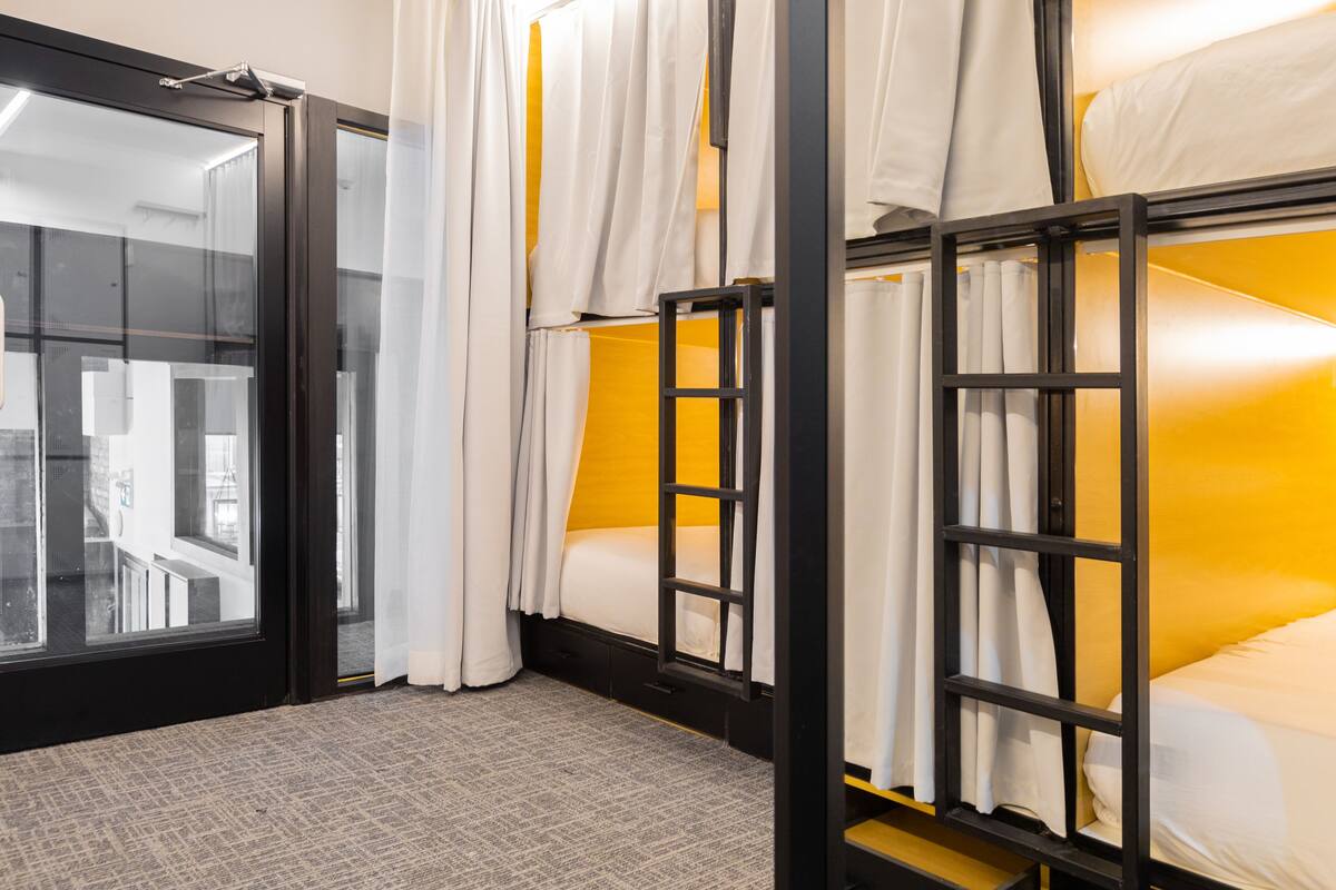 Une chambre avec des lits superposés, une fenêtre avec des rideaux et une vue sur l’extérieur.