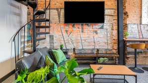 Un interior moderno con pared de ladrillo, televisor montado, escalera, sofá, mesa de centro y una planta pequeña.