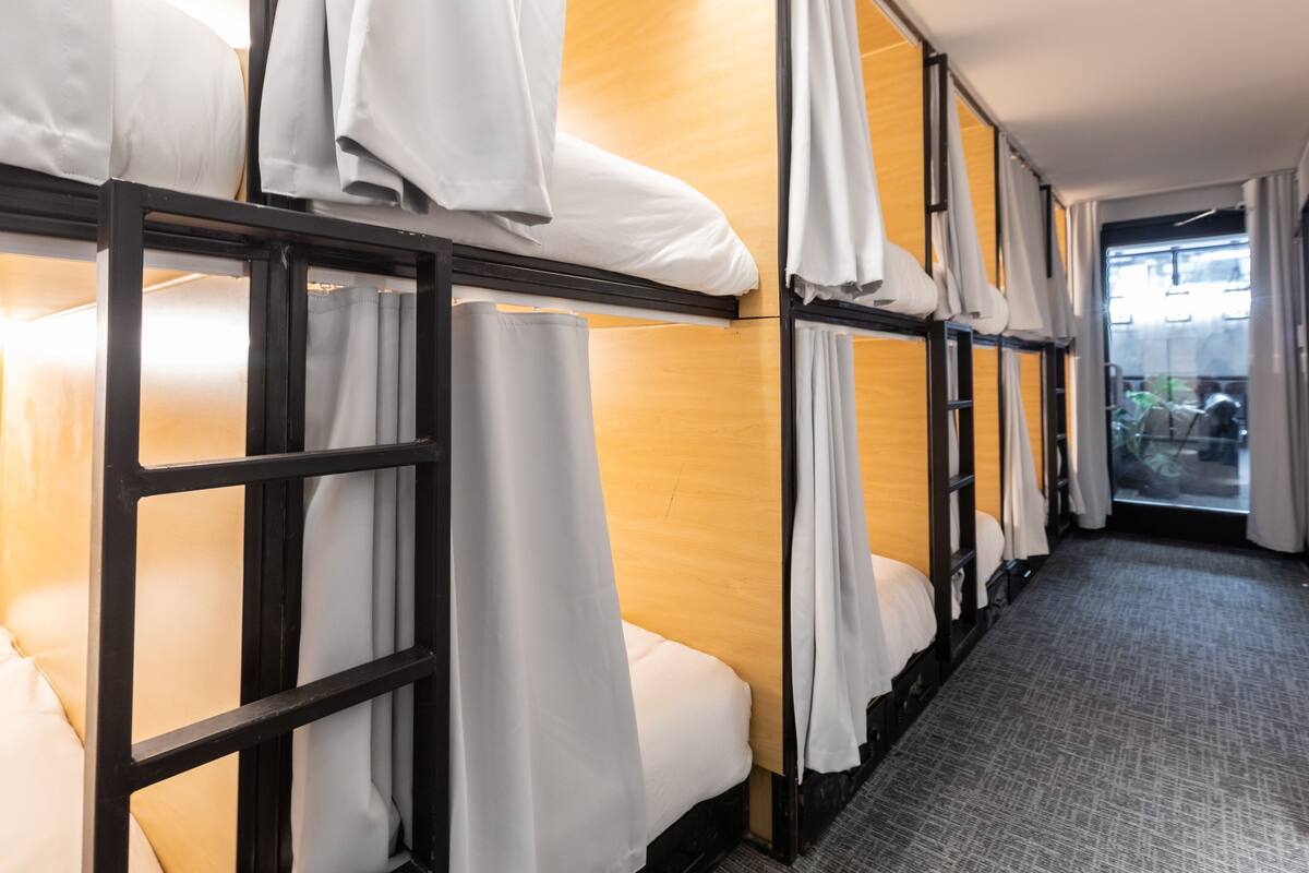 Une chambre d’hôtel avec des lits superposés, chacun étant équipé de draps et de rideaux blancs.