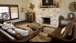A living room with a stone fireplace, leather sofas, a television, and a chessboard. - Experience the West Texas Rockies (Guthrie)