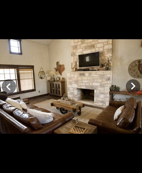 A living room with a stone fireplace, leather sofas, a television, and a chessboard. - Experience the West Texas Rockies (Guthrie)