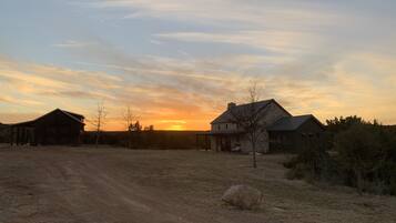 A rural landscape with a dirt road, a barn, and a house during sunset.