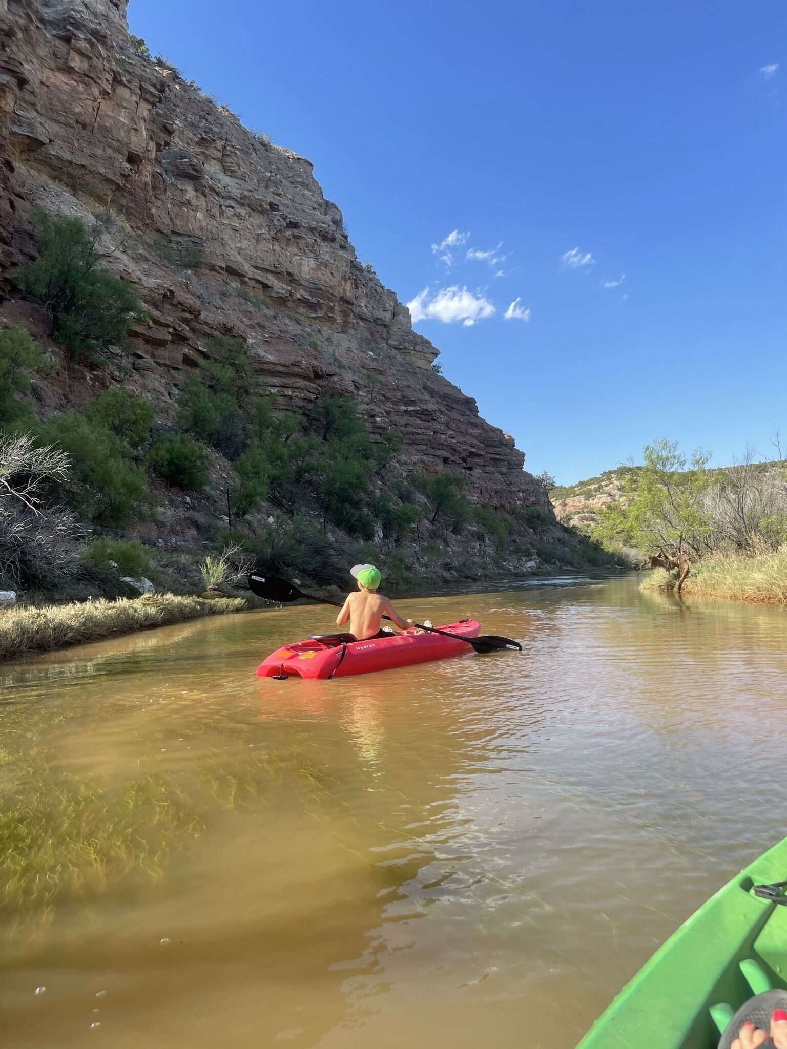 A kayaker in a red kayak on a calm river with a rocky cliff on one side.