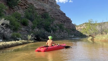 A kayaker in a red kayak on a calm river with a rocky cliff on one side.