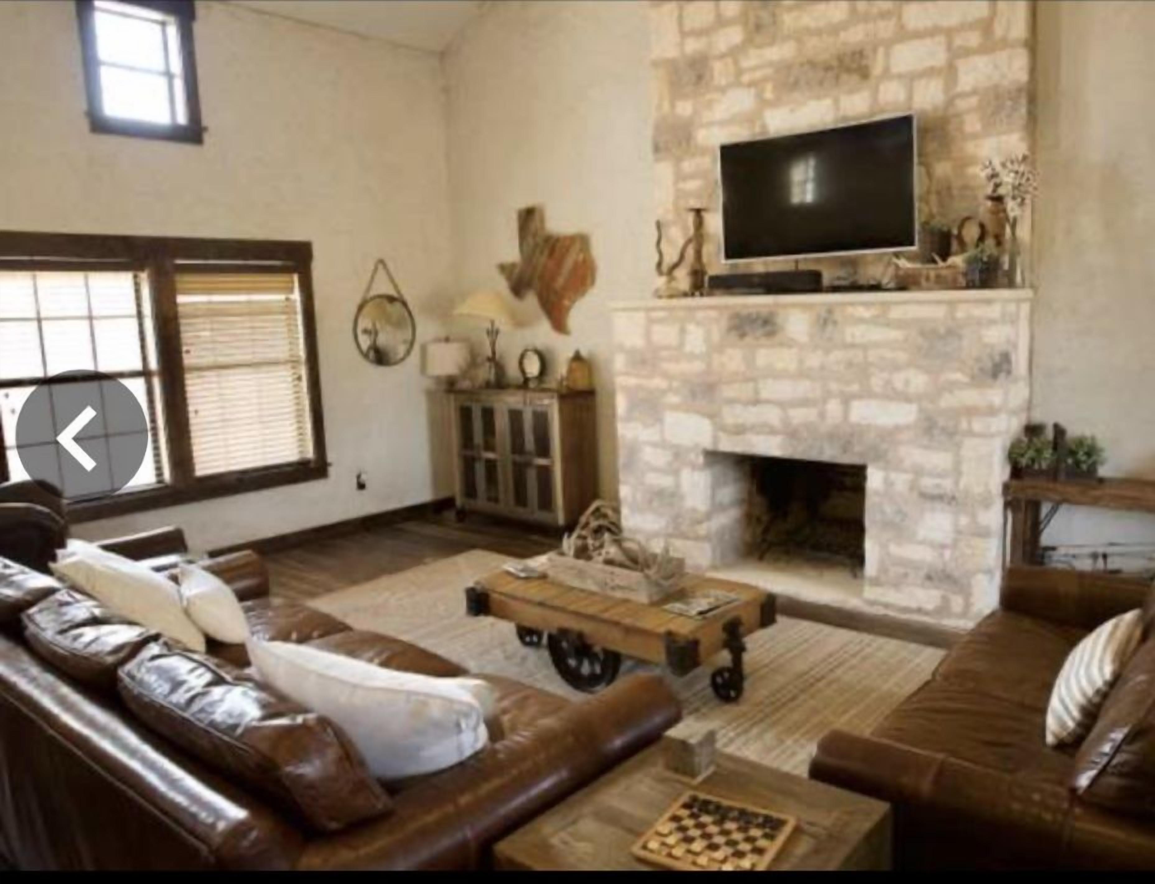 A living room with a stone fireplace, leather sofas, a television, and a chessboard.