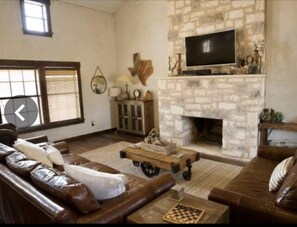 A living room with a stone fireplace, leather sofas, a television, and a chessboard. - Experience the West Texas Rockies (Guthrie)