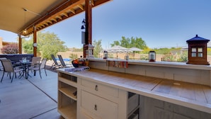 Een buitenkeuken met een bargedeelte, stoelen en een pergola.