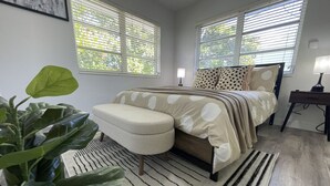 A bedroom with a bed, a nightstand, a lamp, a large plant, and a window with blinds. - 2655 SW - APT 3 · Great Apart near CocoWalk & Brickell w/parking! (Miami)