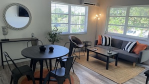 A modern living room with a round dining table, black chairs, a sofa with striped cushions, and a large mirror on the wall. - 2655 SW - APT 3 · Great Apart near CocoWalk & Brickell w/parking! (Miami)