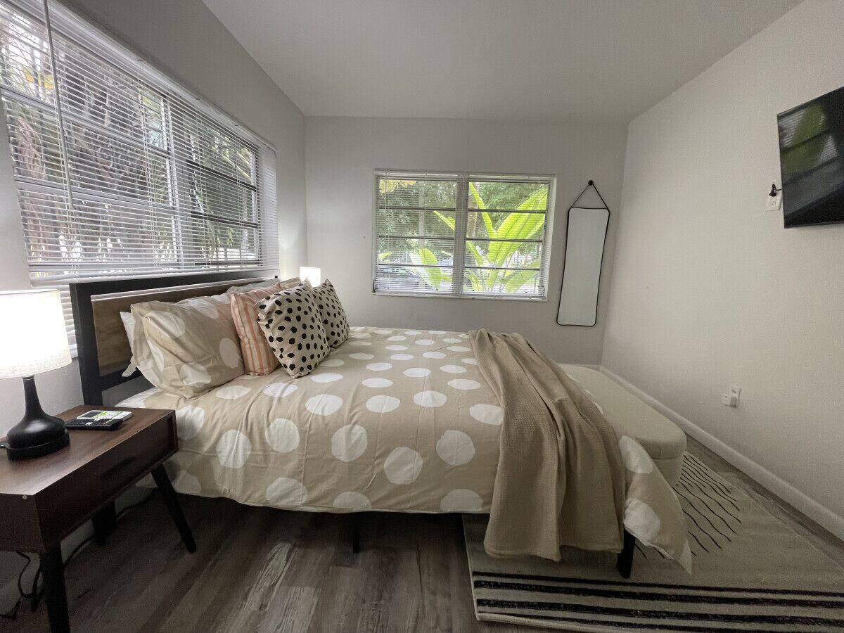 Un dormitorio con cama, mesita de noche, lámpara y ventana con persianas.