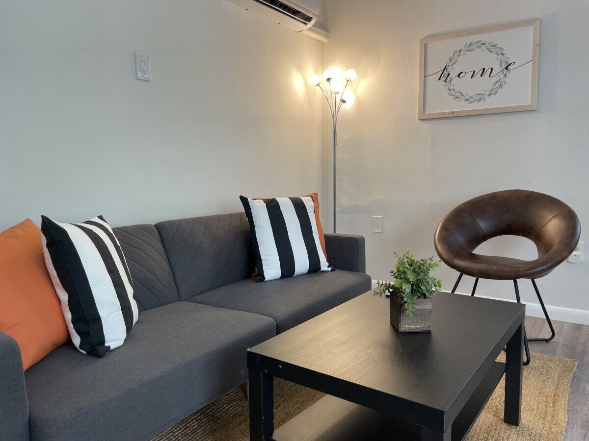 A modern living room with a grey sofa, black and white striped pillows, a black coffee table, a floor lamp, and a brown chair.