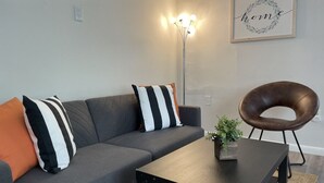 Een moderne woonkamer met een grijze bank, zwart-wit gestreepte kussens, een zwarte salontafel, een potplant en een lijst met het woord 'home'.
