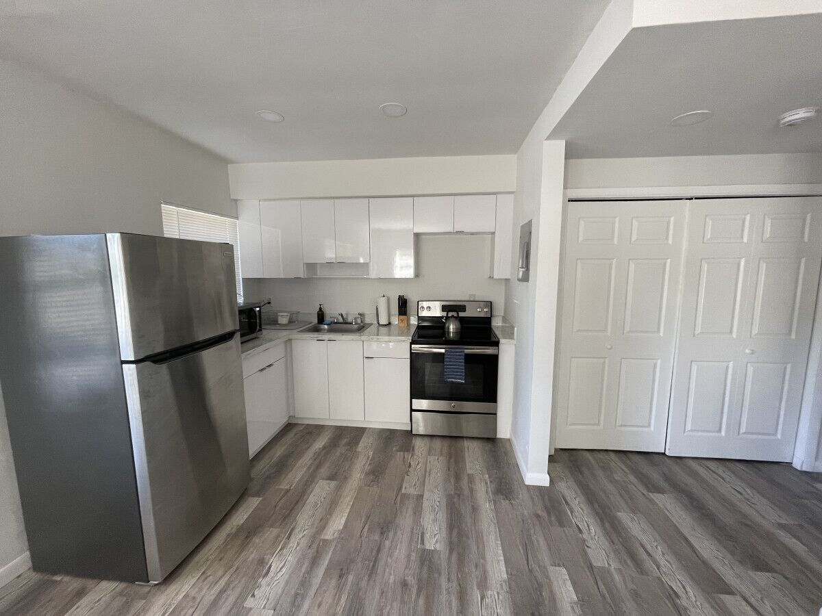 A modern kitchen with white cabinets, stainless steel appliances, and a wooden floor.