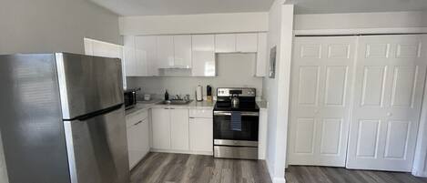 A modern kitchen with white cabinets, stainless steel appliances, and a wooden floor.