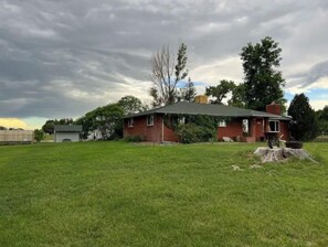 Situated in a serene yard, this charming house features a cozy front porch with a bench and table.