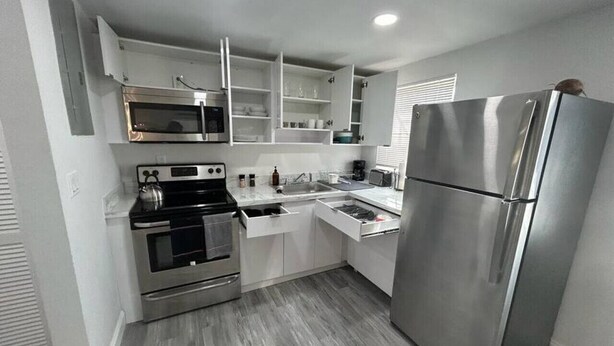 Una cocina moderna con electrodomésticos de acero inoxidable, armarios blancos y piso gris.