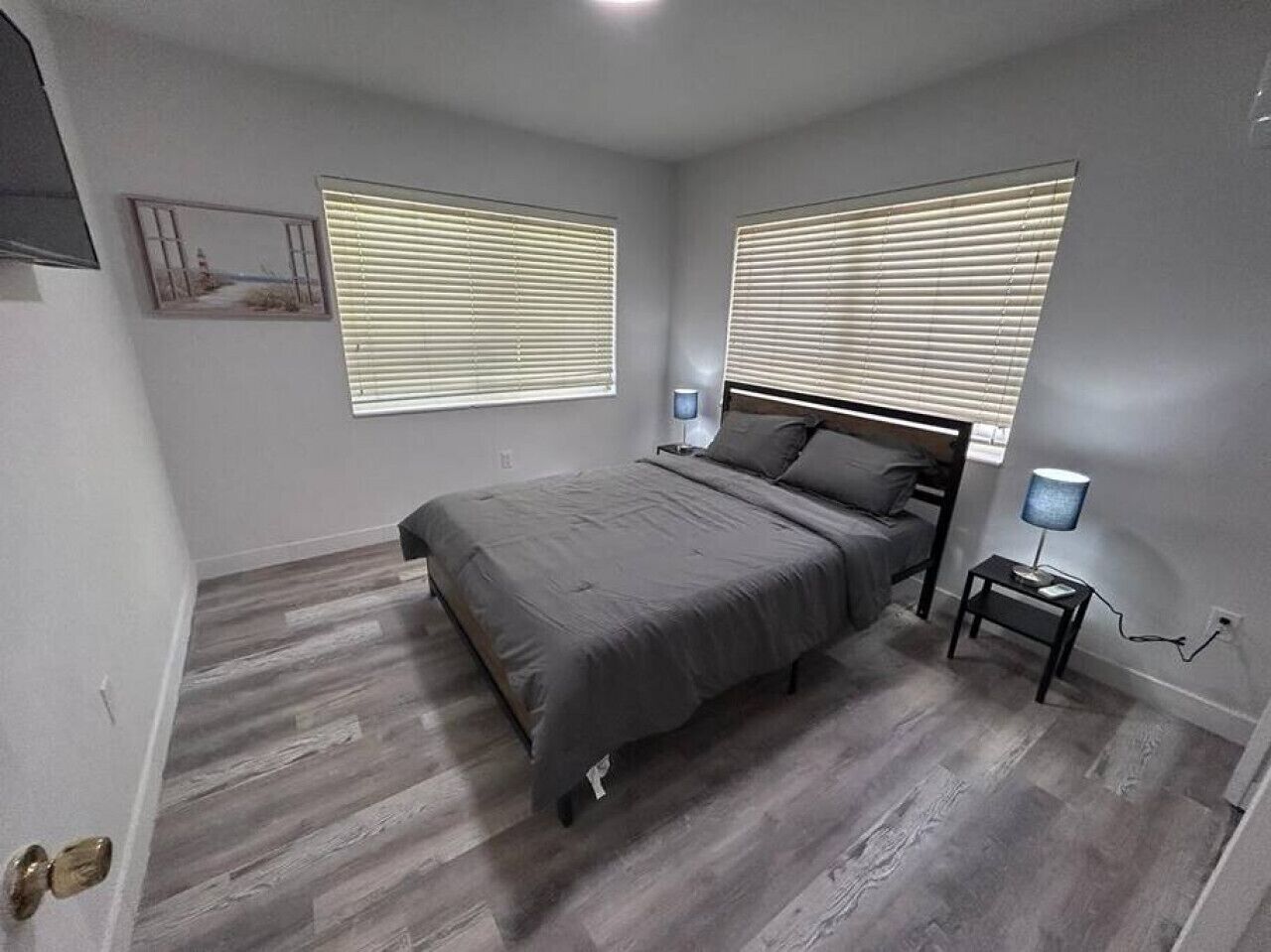 A bedroom with a bed, two bedside tables, a nightstand, and a wall-mounted lamp.