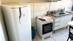 A compact kitchen with a white refrigerator, a small oven, a microwave, and a gas cylinder. - CONDOMÍNIO SONHARE - 202 (Anapolis)