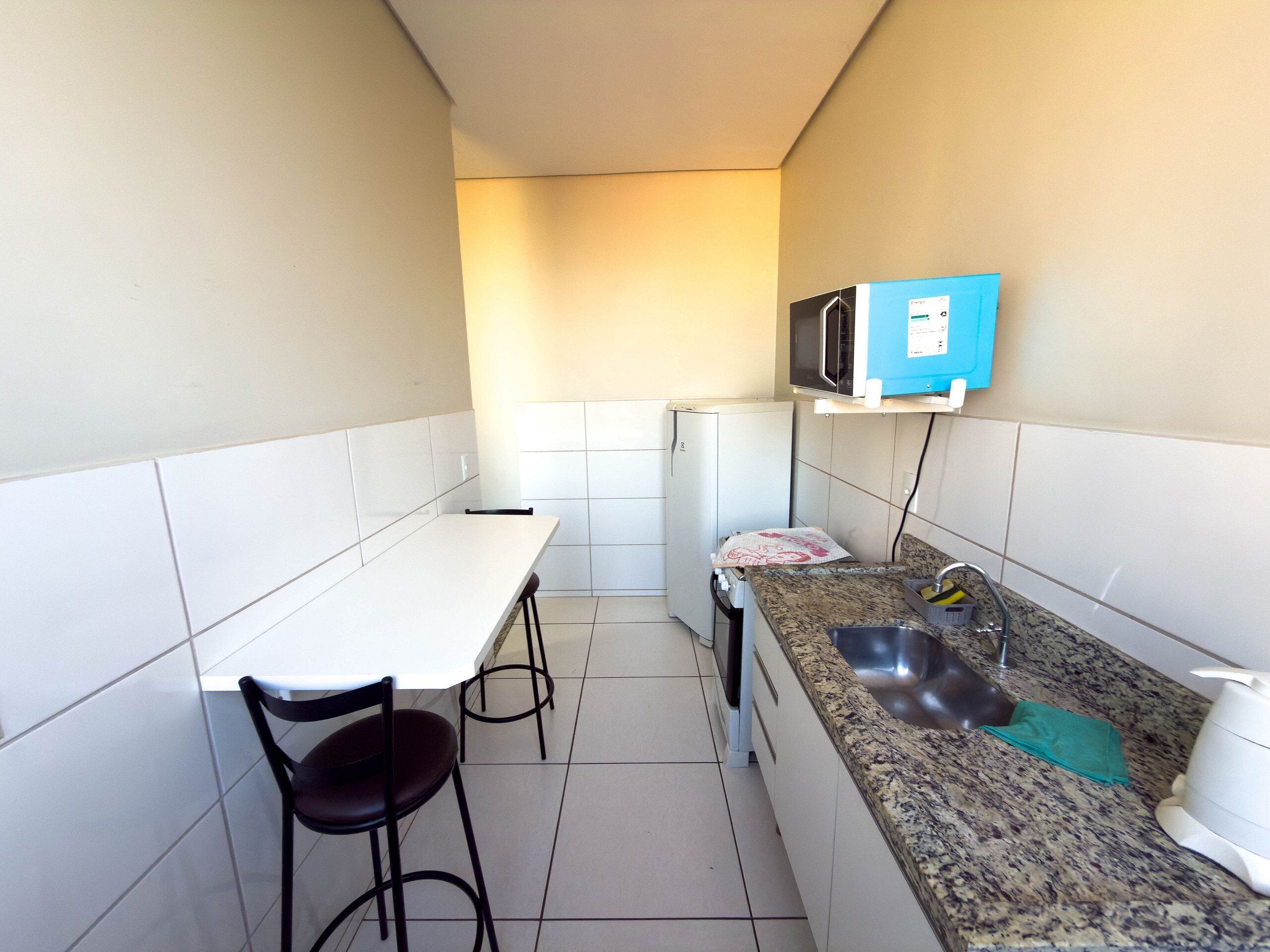 Une cuisine de taille réduite, dotée d’un plan de travail blanc, d’un évier, d’un four à micro-ondes et d’un réfrigérateur.
