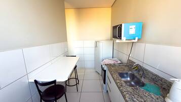Une cuisine de taille réduite, dotée d’un plan de travail blanc, d’un évier, d’un four à micro-ondes et d’un réfrigérateur.