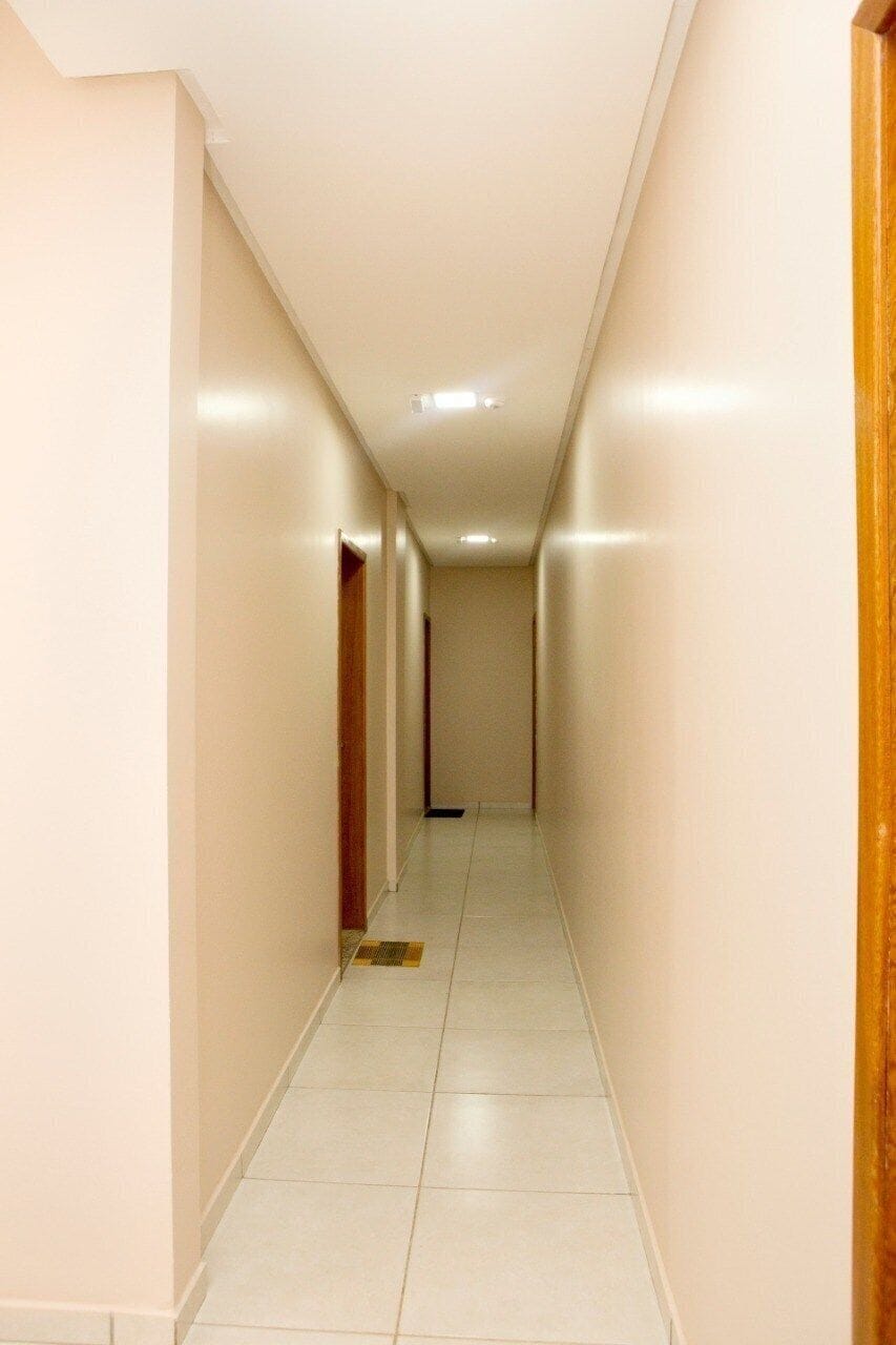 Un pasillo estrecho y bien iluminado, con suelo de baldosas y puertas de madera a ambos lados.