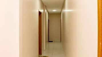 Un pasillo estrecho y bien iluminado, con suelo de baldosas y puertas de madera a ambos lados.