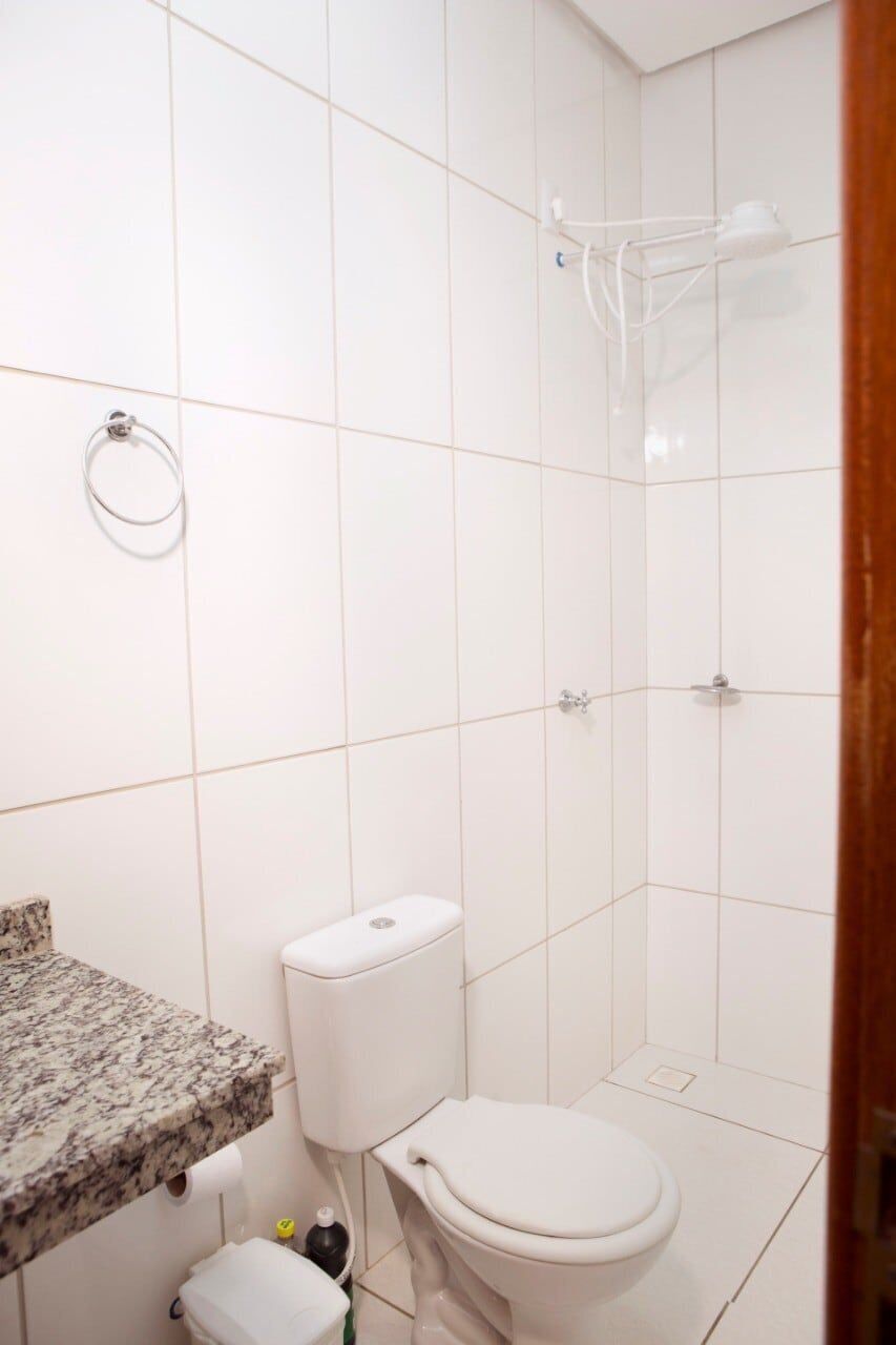 Casa de banho com azulejos brancos, sanita, lavatório com bancada de mármore e zona de duche.