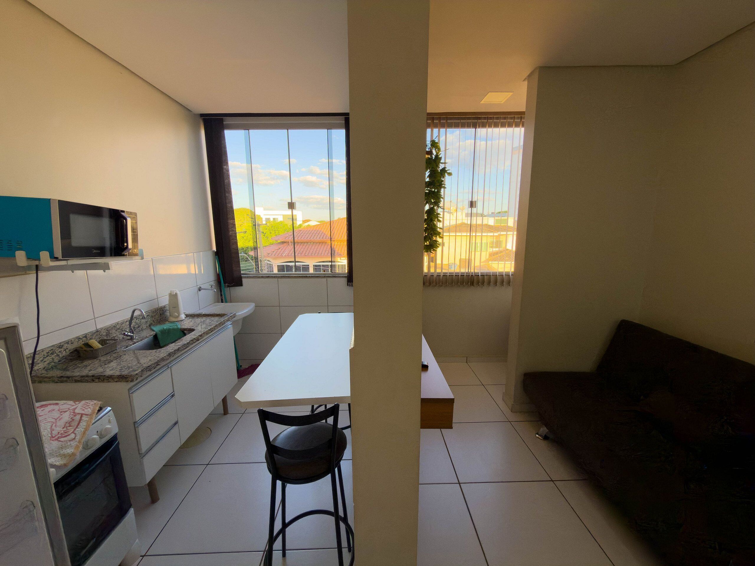 A compact kitchen with a microwave, sink, and stove, a dining area with a table and chairs, and a view through a window.