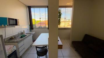A compact kitchen with a microwave, sink, and stove, a dining area with a table and chairs, and a view through a window.