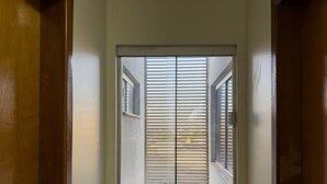 A window with horizontal blinds, a door frame, and a small window above it. - CONDOMÍNIO SONHARE - 202 (Anapolis)