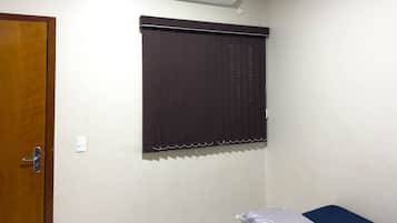 Una habitación con puerta de madera, ventana con persiana oscura y un equipo de aire acondicionado en la pared.