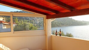 A balcony with a white plastic chair, a wine bottle, and glasses on the windowsill.