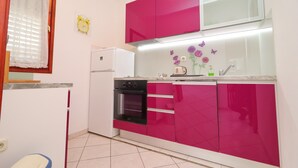 A compact kitchen with pink cabinets, a white refrigerator, and a built-in oven.
