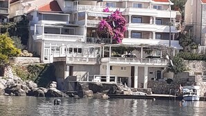 Um edifício costeiro com varandas, base de pedra e vista para o mar.