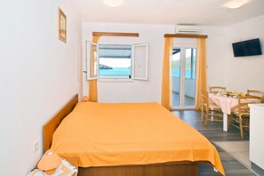 Un dormitorio con cama, ventana abierta, zona de comedor con mesa y sillas, y televisor en la pared.