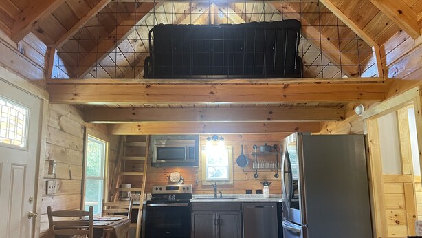 A cozy cabin-style kitchen with wooden walls, a loft area, and basic amenities including a refrigerator, stove, and microwave. - The Stillhouse Cabin, mins from Red River Gorge (Campton)