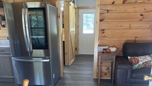 A wooden cabin interior with a stainless steel refrigerator, a wooden dining table with a pumpkin decoration, and a dark wooden floor. - The Stillhouse Cabin, mins from Red River Gorge (Campton)