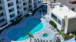 A rooftop pool with a curved design, surrounded by lounge chairs and palm trees, adjacent to a modern building with balconies. - Charming Waterfront 1/1.5 Beautiful Sunsets at the Strand! (Sarasota)