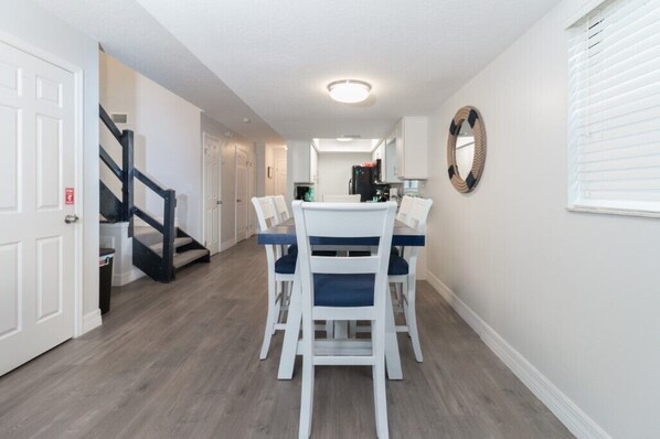 A dining area with a table and chairs, a staircase, and a kitchen in the background.