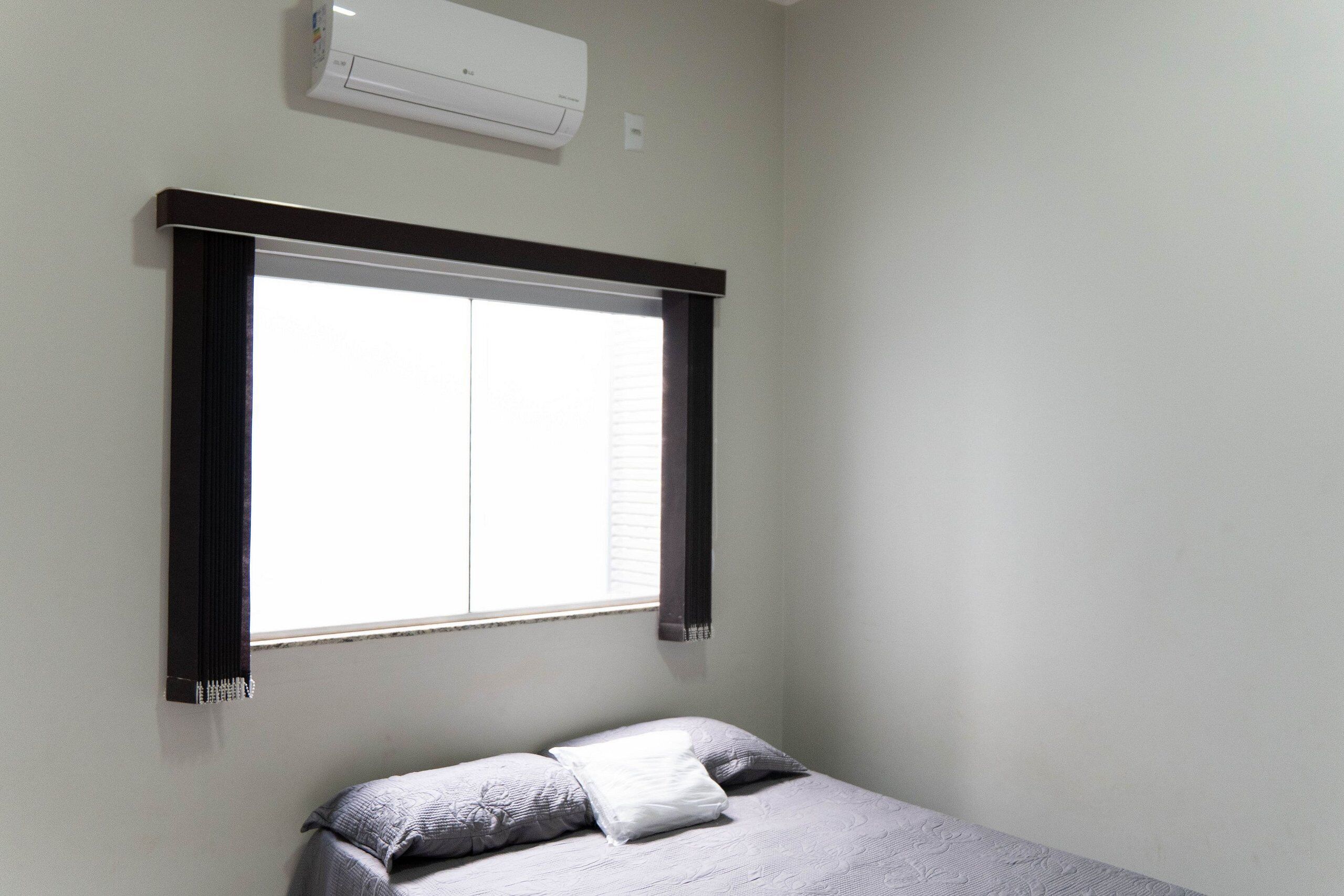 Quarto com cama, janela com persianas e ar condicionado na parede.